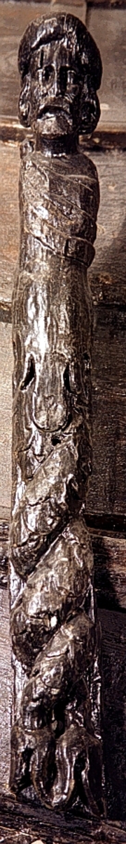 Skulpterad Triton med tjock lagerkrans på huvudet.
Figuren har stora yviga mustascher och långt, lockigt hår. Snett över bröstet är en klädnad draperad. Klädnaden är hopfäst på vänster axel.

Övergången till de snodda fiskstjärtarna döljs av ett stort, flikigt blad vars mittflik är förtjockad och upprullad. Skulpturens fotända är tapp- eller kilformad och tillplattad från sidorna. Tritonens huvud är framställt som rundskulptur. Från axlarna och nedåt är baksidan slät och plan. I höjd med övergången till stjärtpartiet finns ett kraftigt urtag. Nedtill bryter baksidans fotända av inåt.

Text in English: Sculpted Triton with thick laurel wreath on its head.
The figure has a large bushy moustache and long curly hair. A garment is draped across the chest and fastened on the left shoulder.

The transition between the upper body and fish tails is concealed by a large leaf, the middle segment of which is thickened and rolled up. The foot end of the sculpture has a flat end, seen from the side, and is wedge-shaped. The Triton''s head is carved as a three-dimensional sculpture. The rear side is smooth. There is a deep groove on the rear side at the transistion point between the male torso and the fish tails.