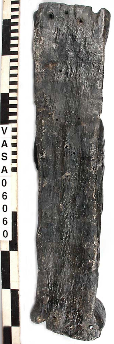 Skulptur föreställande en barnfigur som spelar på en sinka (ett äldre blåsinstrument med grepphål som blockflöjten men ett munstycke som liknar trumpetens).
Huvudet är vridet något åt höger. Kroppstyngden vilar på höger ben medan vänster ben är böjt. Instrumentet hålls med båda händerna. Skulpturen förefaller delvis draperad i en mantel eller dylikt som skymtar vid hans högra sida. Ovanför hjässan syns en något snedställd äggstavslist. Figuren står på ett minimalt underlag som troligen avser att föreställa ett stycke naturlig mark. Skulpturens baksidan är slät.
Skulpturen är kraftigt sliten.

Text in English: A sculpture of a child playing a sinka.
The weight of the body rests on the right leg while the left is bent and the head is turned slightly to the right.. The instrument is held in both hands. The figure seems to be partly draped in a cloak or the like, which conceals his right side. Just above the head the back board comes forward at right angles and the front of the board is decorated with an egg  mould design. The sculpture stands on a small flat plinth. The back of the sculpture is smooth.
The sculpture is very worn.