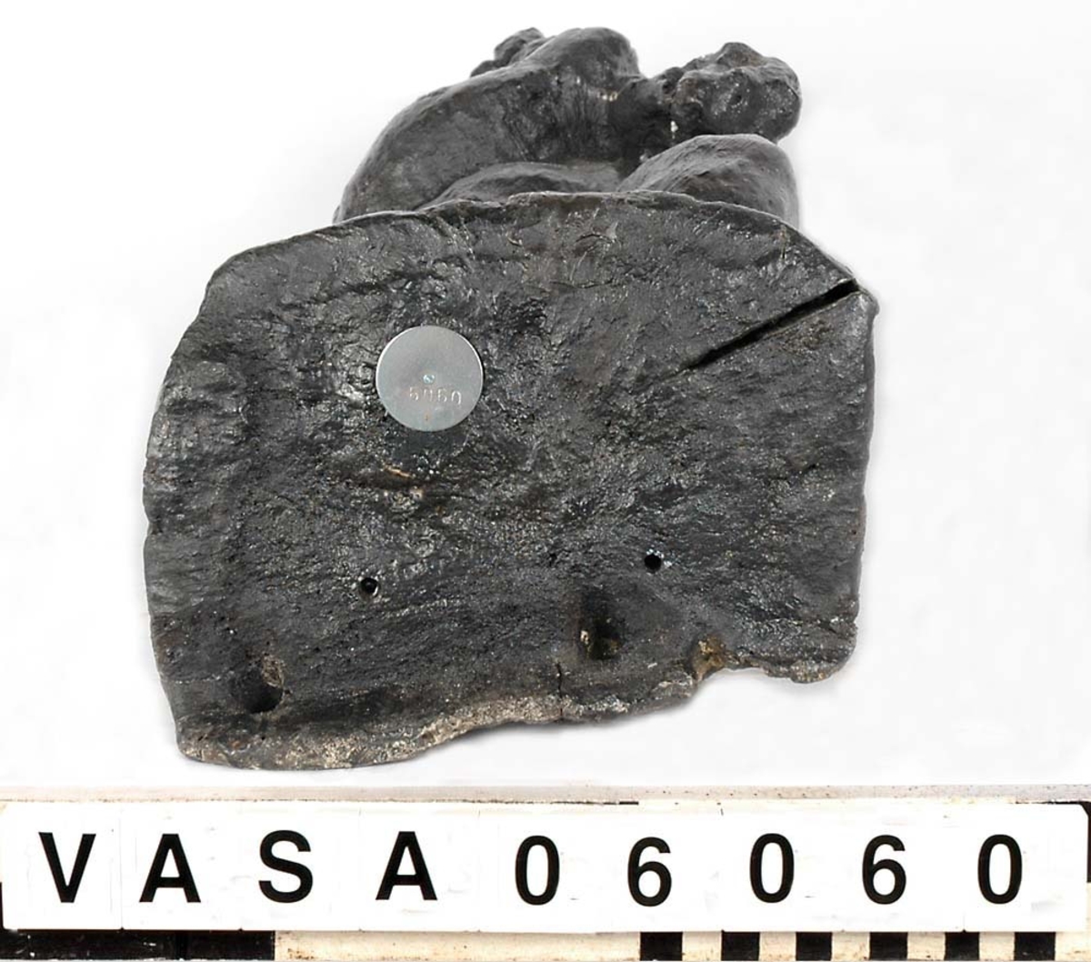 Skulptur föreställande en barnfigur som spelar på en sinka (ett äldre blåsinstrument med grepphål som blockflöjten men ett munstycke som liknar trumpetens).
Huvudet är vridet något åt höger. Kroppstyngden vilar på höger ben medan vänster ben är böjt. Instrumentet hålls med båda händerna. Skulpturen förefaller delvis draperad i en mantel eller dylikt som skymtar vid hans högra sida. Ovanför hjässan syns en något snedställd äggstavslist. Figuren står på ett minimalt underlag som troligen avser att föreställa ett stycke naturlig mark. Skulpturens baksidan är slät.
Skulpturen är kraftigt sliten.

Text in English: A sculpture of a child playing a sinka.
The weight of the body rests on the right leg while the left is bent and the head is turned slightly to the right.. The instrument is held in both hands. The figure seems to be partly draped in a cloak or the like, which conceals his right side. Just above the head the back board comes forward at right angles and the front of the board is decorated with an egg  mould design. The sculpture stands on a small flat plinth. The back of the sculpture is smooth.
The sculpture is very worn.