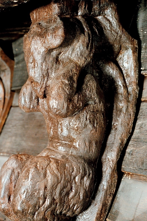 Skulptur föreställande en djävulsfigur i starkt hukande ställning, placerad på en hög sockel.
Figurens huvud är utrustat med stora, krumma horn. I vardera handen håller den på ömse sidor av huvudet något som möjligen kan tolkas som en stor snäcka eller lur. Hakan pryds av ett bockskägg. Figuren har fladdermusvingar på ryggen och starkt luden underkropp med klövförsedda bockfötter. Fötterna vilar på den starkt sluttande sockeln, som framtill är prydd med en ap- eller lejonliknande maskaron med stor nos och hög, välvd panna. På sockelns sidor ses voluter.
Sockeln utgör fortsättning på det kraftiga klink-konstruerade bakstycket som är framdraget ovanför figuren.
Skulpturen är delvis kraftigt sliten och vittrad, särskilt den övre delen. Nederdelen är något bättre bevarad.

Text in English: Sculpture of a devil figure in a crouched position, placed on a high socle.
The figure''s head is equipped with large, curved horns. In either hand the figure holds on either side of its head something that may possibly be identified as a large seashell or horn. The devil has a goat''s beard on its chin, bat wings on its back and very hirsute lower parts of the body, and cloven goats'' feet.
The feet rests on a sharply sloping socle that is decked in front with a mask of an ape-like or lion-like face with a large nose and a high arched forehead. On the sides of the socle volutes are visible.
The socle forms the extension of the heavy, clinker-built back-piece, which is drawn forward above the figure.
The sculpture, particularly its upper parts, is much worn and disintegrated. The lower part is somewhat better preserved.