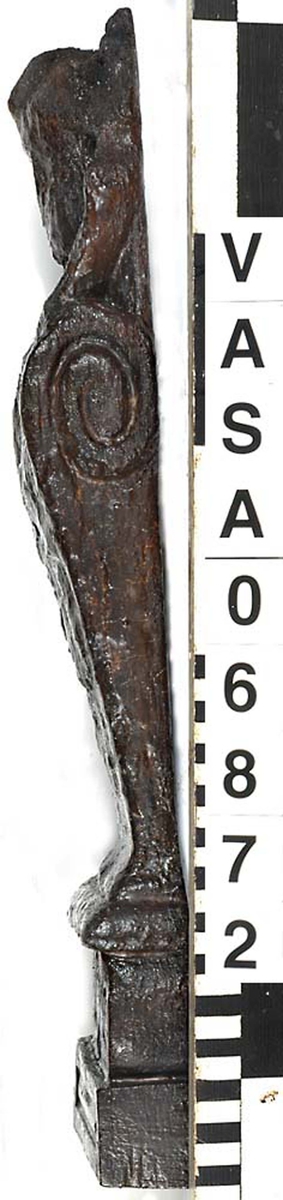 Liten skulpterad pilaster, troligtvis utformad som en karyatid eller möjligen en putto. Figuren har långt hår och ett knubbigt ansikte, omgivet av en bred krage. Det nedåt avsmalnande pilasterskaftet är dekorerat med akantusblad. Nedtill avslutas pilastern av en rikt profilerad och dekorerad sockel. Skulpturens baksida är slät.

Skulpturen är sliten, pilasterns nedre del är dock mindre sliten än den övre.



Text in English: A small carved pilaster, with a caryatid or probably a putto. The figure has a chubby face, long hair and a broad collar. The lower part of the pilaster is decorated with acanthus leaves. The caryatid stands on a richly profiled and decorated socle. The back of the sculpture is smooth.

The sculpture is worn, the lower end less so than the upper.