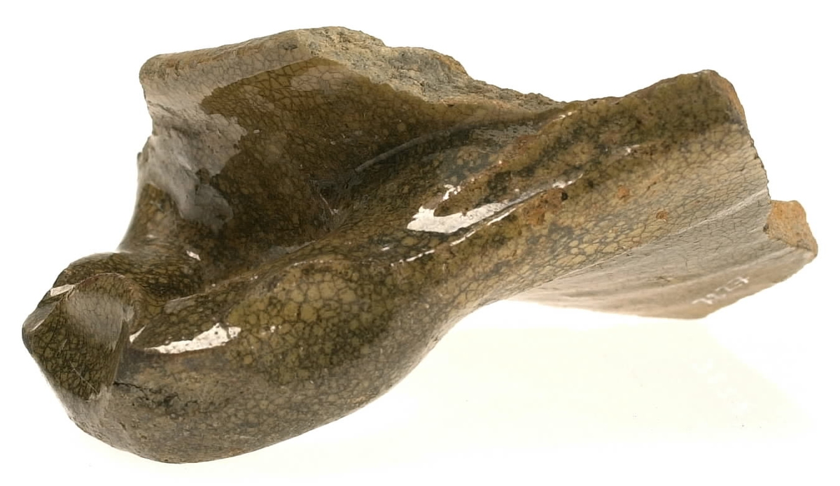 Del av skål.
1 st vertikal bandhänkel, tummad, 70 x 60 mm. Fragment av mynningsrand och buk. In- och utsida blyglaserad gulgrön.