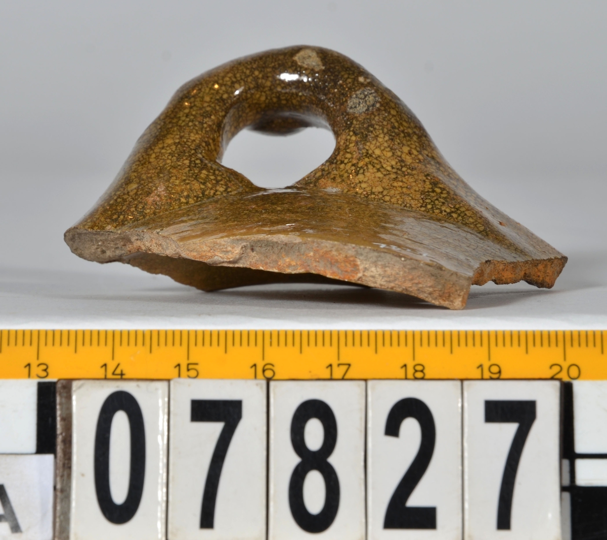 Del av skål.
1 st vertikal bandhänkel, tummad, 70 x 60 mm. Fragment av mynningsrand och buk. In- och utsida blyglaserad gulgrön.