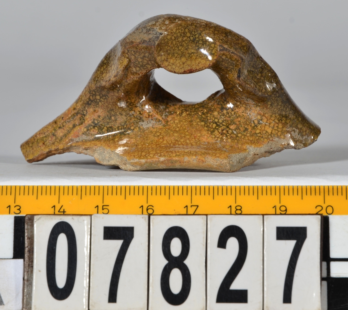 Del av skål.
1 st vertikal bandhänkel, tummad, 70 x 60 mm. Fragment av mynningsrand och buk. In- och utsida blyglaserad gulgrön.