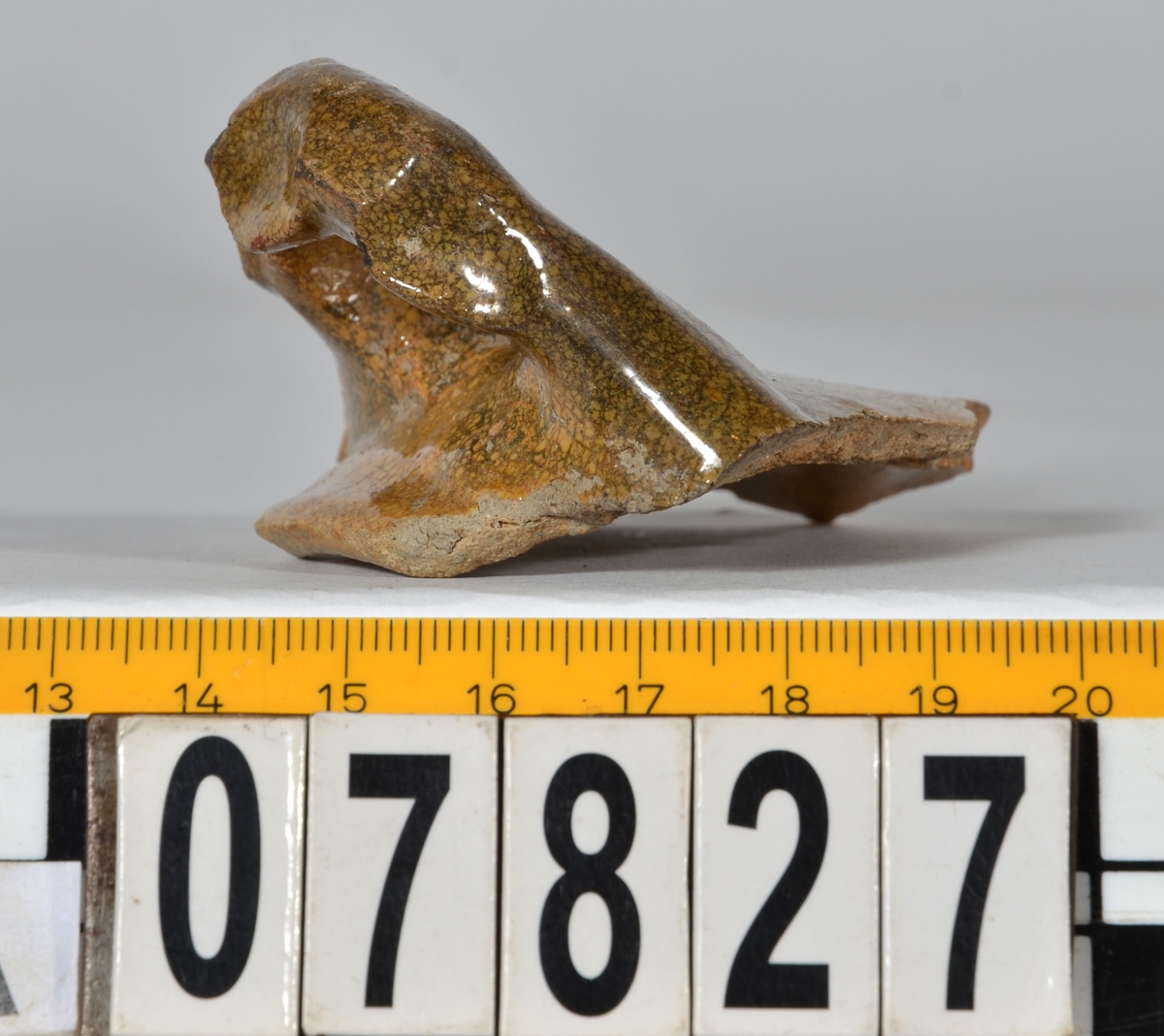 Del av skål.
1 st vertikal bandhänkel, tummad, 70 x 60 mm. Fragment av mynningsrand och buk. In- och utsida blyglaserad gulgrön.