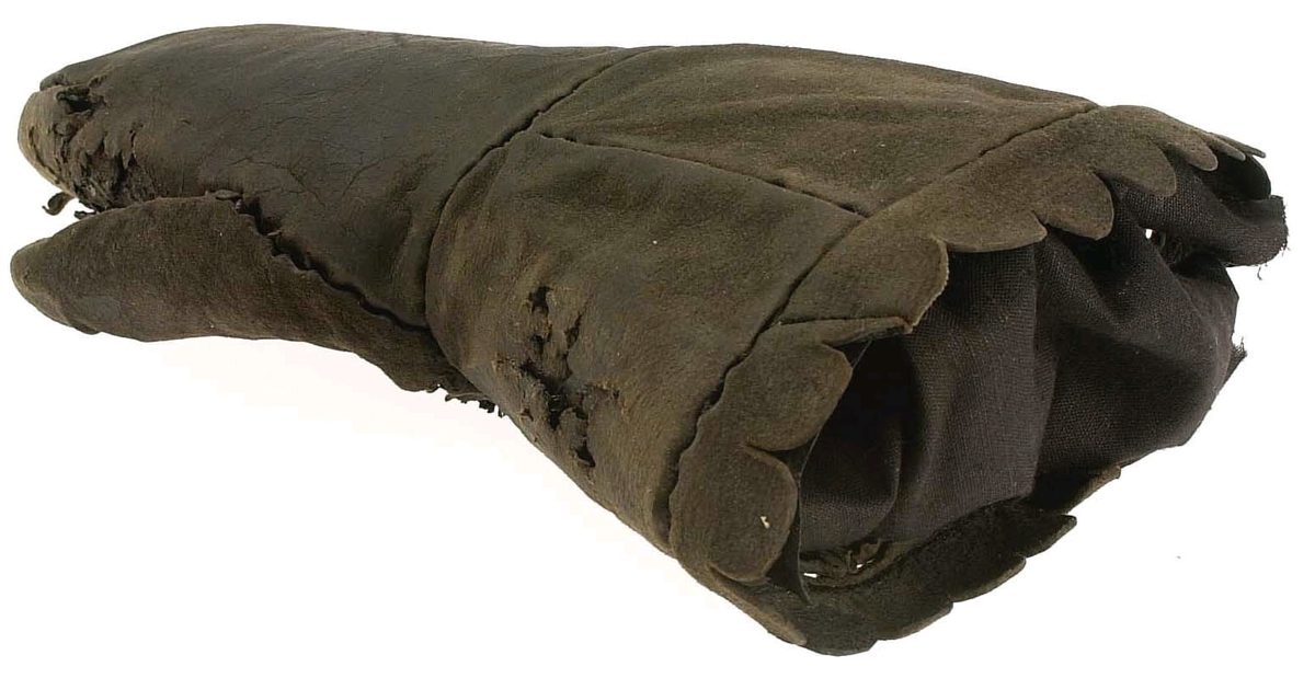 En kragvante till höger hand. Sydd av flera kraftiga läderstycken. Påsydd bård i ett stycke i form av rundade "tungor" längs kragkanten.