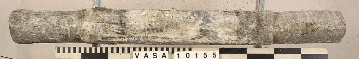 Lavettaxel, främre. Ett avlångt trästycke med kvadratiskt tvärsnitt mitt på samt cylinderformade ändar. Axeln var fastsatt i lavettbottnens undersida med två grova spikar och två järnband.

För mer information se Dokumentationsblankett under Referenser – Länkade filer.

Text in English: Axle (front) for gun carriage 10153, consisting of a square-section beam with round stub axles at the ends, originally fixed to a notch in the underside of the carriage bed by two nails and two iron straps.

For more information see the Documentation form under References – Linked files.