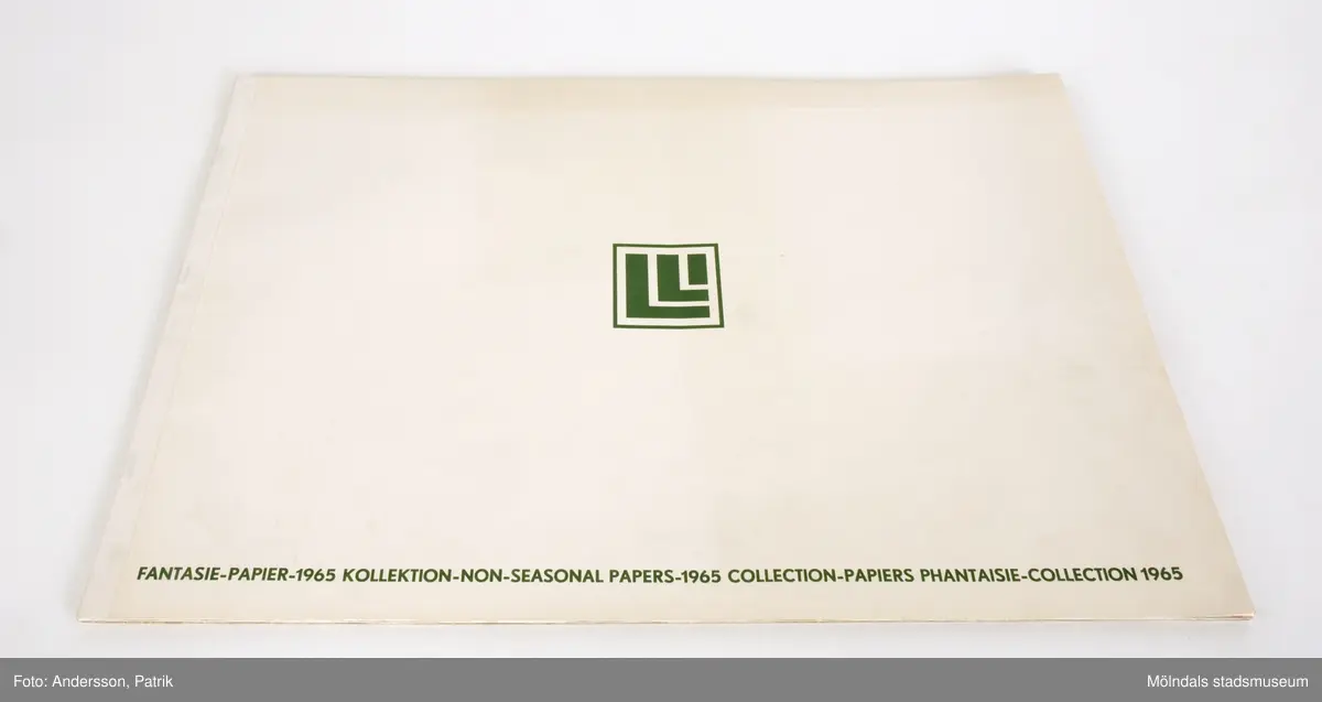 1st bok/häfte med flera pappersprover med olika mönster och motiv.Dassa pappersprover kan ha varit prover för Presentpapper, Kökslådepapper eller Bordsdukar.Varje pappersark har ett motiv eller mönster. På baksidan av varje ark står det ett nummer och vad det är för möster.Omslaget av pappersprovboken är vitt. På framsidan längst ner står det tryckt med mörkgröna bokstäver: "FANTASIE-PAPIER-1965 KOLLEKTION-NON-SEASONAL PAPERS-1965 COLLECTION-PAPIERS PHANTASIE-COLLECTION 1965"Det finns också en mörkgrön logga i mitten av framsidan.Storlek på pappersprovsboken:Längd: 335 mmBredd: 486 mmDjup: 4 mm