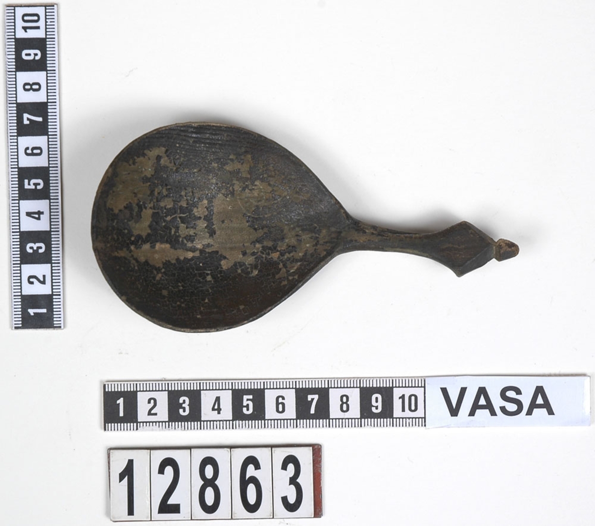 En träsked. Skeden har ett ovalt skedblad och ett kort skaft. Skaftets ände är rombformat samt försett med en liten knopp. På skedbladet syns en inristad dekor.

Skeden är välbevarad och har synliga färgspår.

För mer information se Dokumentationsblankett under Referenser – Länkade filer.