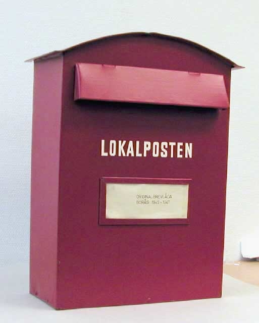 Brevlåda, röd, märkt Lokalposten. Brevlådan har rundat tak
och är försedd med klaff för brevinkastet samt ett anslagsfönster.
Brevinkastets  mått: L = 300 mm, H = 37 mm.