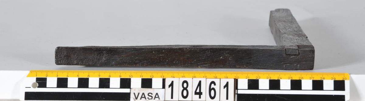 En vinkelhake.

Vinkelhaken består av två plana stavar som är sammanfogade genom sinkning. Ändarna är profilerade. I mitten av den kortare staven finns ett runt hål för upphängning.

Vinkelhaken är välbevarad och i gott skick.

För mer information se Dokumentationsblankett under Referenser – Länkade filer.