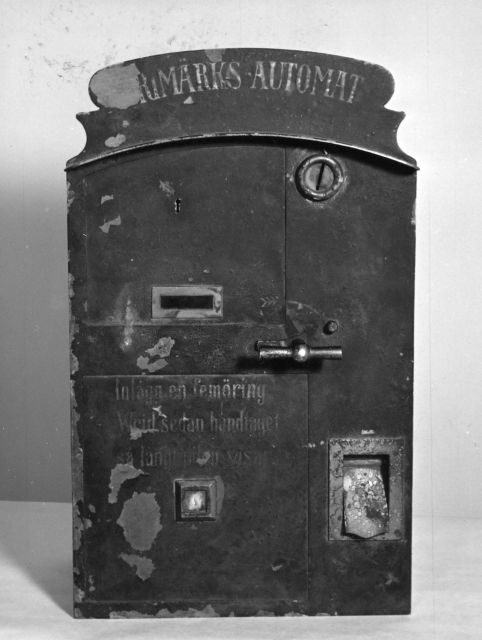 Frimärksautomat för 5-öres frimärken. Mörkblå med vit text:
Inlägg en 5-öring och vrid sedan handtaget så långt pilen visar.