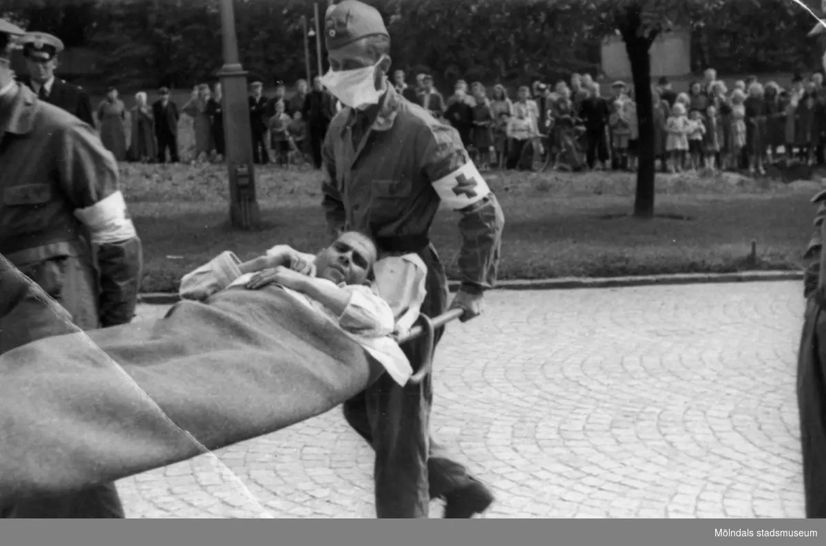 "Karantänsförläggning" på Kvarnbyskolan för överlevande från koncentrationsläger i Tyskland och Polen 1945.  
Skolan fungerade under denna sommar som beredsskapssjukhus.

Manlig flykting blir buren på bår av Röda Korsets personal.