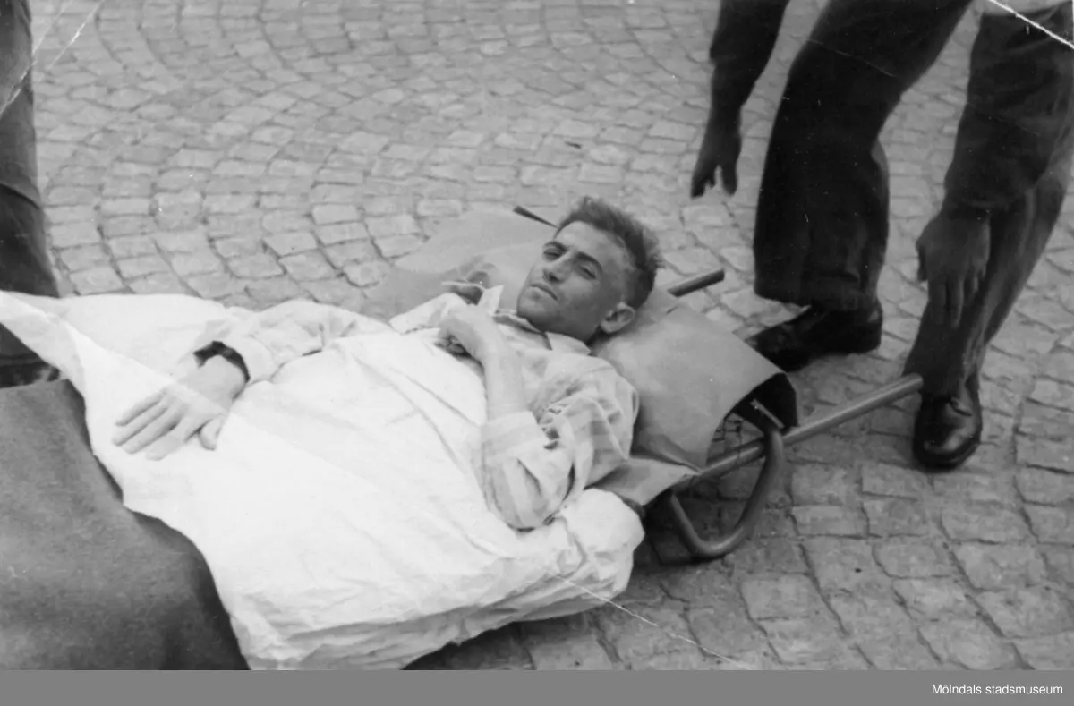 "Karantänsförläggning" på Kvarnbyskolan för överlevande från koncentrationsläger i Tyskland och Polen 1945.  
Skolan fungerade under denna sommar som beredsskapssjukhus.
 
Manlig flykting som bärs på bår.