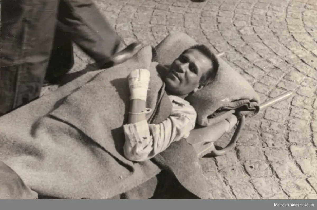 "Karantänsförläggning" på Kvarnbyskolan för överlevande från koncentrationsläger i Tyskland och Polen 1945.  
Skolan fungerade under denna sommar som beredsskapssjukhus.

En manlig flykting på bår, buren av Röda Korsets personal.