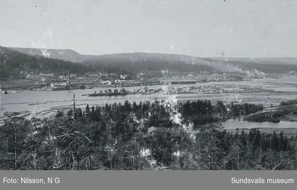 Vy över Svartviks hamnområde med sågverk,  magasinbyggnader och uppläggningsplatser för timmer.I bakgrunden olika bostadstyper.