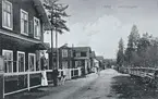 Alby - Järnvägsgatan. Motivet visar i förgrunden den byggnad som senare kom att bli Alby Hotell. Fastigheten (Hotellet) ägdes 1906-1918 av Jonas Fredrik Hamrin som hade ett café på hörnet. Byggnaden i bildens mitt ägdes av Nils Jonas Eriksson som även han drev ett café. Den byggnaden lär för övrigt vara den första som byggdes (1898) på västra sidan om järnvägen. Vykort.