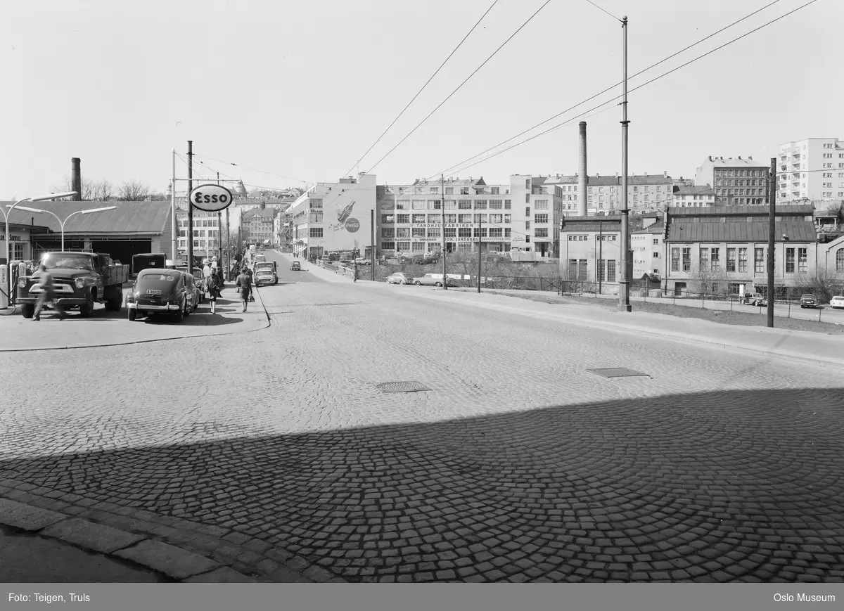 gateløp, Esso bensinstasjon, fabrikkbygninger, bygårder, biler, mennesker, gateliv, gatelegeme, brostein