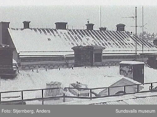 Bild 05 Rivning av takstolar norra mittpartiet. Taket med falsad plåt och undetaket  av bräder är redan bitvis borta.Bild 06 Detalj av stålbalk med stöd mot yttervägg i norr.Bild 08-09 Överbyggnaden inifrån mot sydöst.Bild 16,19 Vy mot frilagd skorsten i söder dvs den dubbla skorstenens högra del.Bild 20-21 Byggnadens norra del fr V.Bild 22 Den bortplockade vapensköldens väggyta på norra fasadens risalit.Bild 23 Vy utmed norra takfallet fr V