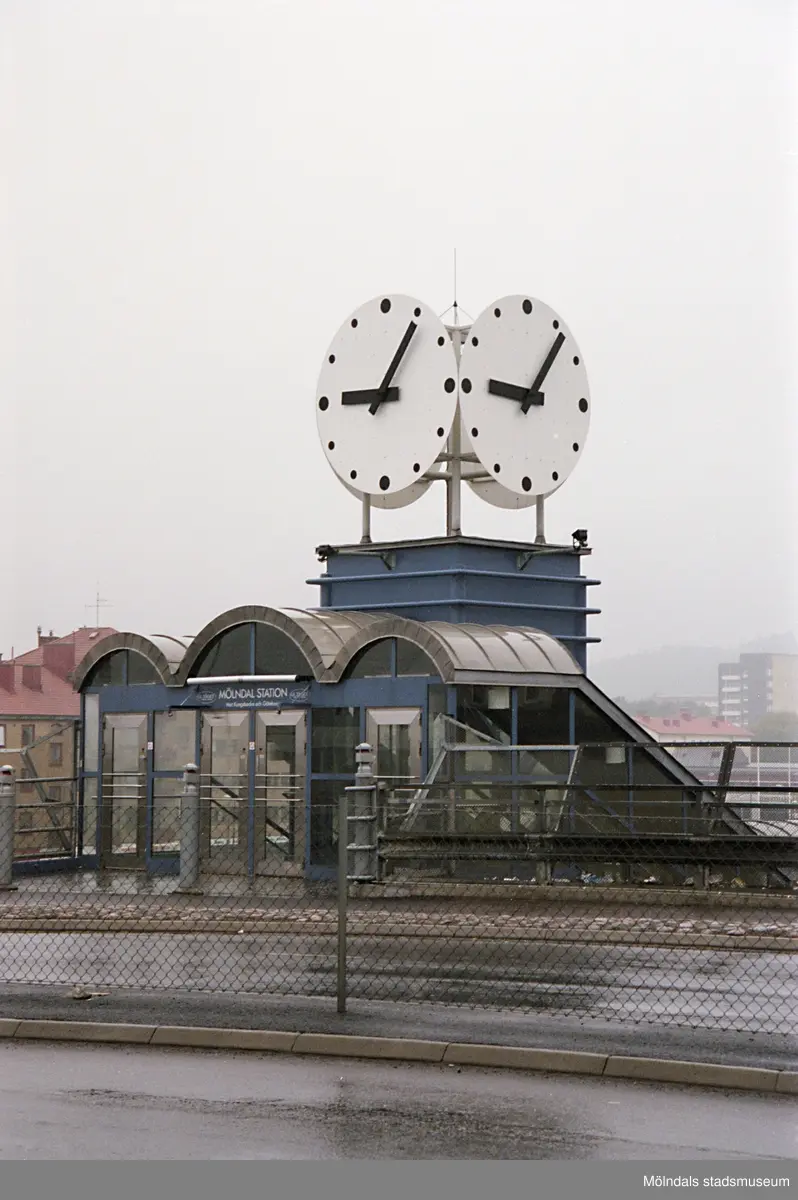 Entré från bron, ner till Mölndal station, med urverk fastsatt på taket. Mölndalsbro i dag - ett skolpedagogiskt dokumentationsprojekt på Mölndals museum under oktober 1996. 1996_1135-1152 är gjorda av högstadieelever från Kvarnbyskolan 9D, grupp 1. Se även 1996_0913-0940, gruppbilder på klasserna 1996_1382-1405 samt bilder från den färdiga utställningen 1996_1358-1381.