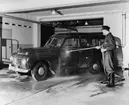 Ett av posttransportörernas dagliga jobb är bilvård under en halvtimme. Chaufför Einar Andersson spolar här lantbrevbärare Nils Liberts blå Volvo herrgårdsvagn i postkontorets Eskilstuna 1 garage.