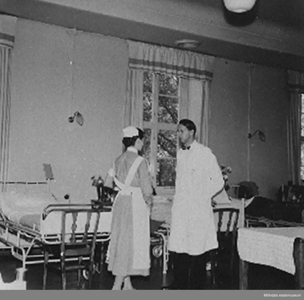 Avdelningsläkare Dr. Bjorwill och assisterande sköterska går rond på Sabbatsbergs sjukhus i Stockholm, cirka 1958. Det låg 20 st patienter i varje sal, 10 st på var sida.