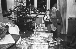 Jultomte med en flicka i knät och julklappar framför sig. Fo