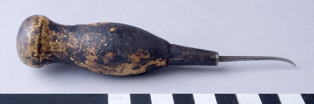 Syl, flatsyl, fabriksgjord av stål, med svarvat handtag av trä. Sylen är fäst i handtaget med hjälp av en metallhylsa och är böjd framtill med slipat platt skär.
Handtaget är delvis täckt med beck.
Märkt otydligt: "..OSS & SON"