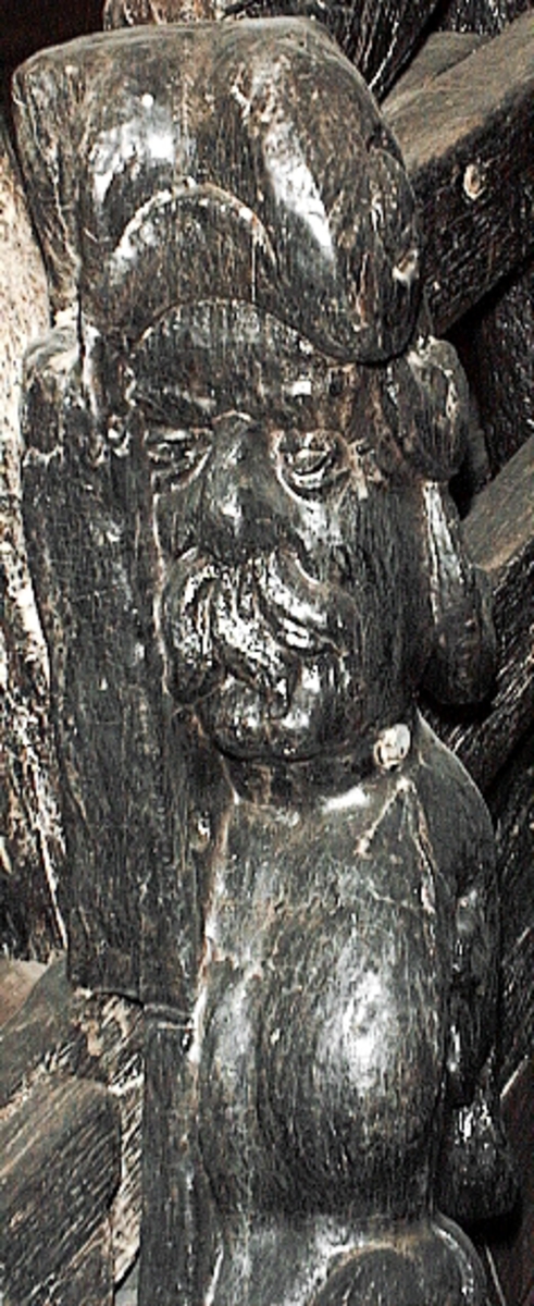 Skulptur av en triton, svängd mot höger.
Tritonen är framställd i vänster profil och avtecknar sig i hög relief mot det släta bakstycket. Tritonen har en stor näsa och treflikig mustasch. På huvudet sitter en hjälm med dekorativa bladvoluter. Armarna är ersatta av långa, flikiga bladslingor. Bålens övergång i den fjällförsedda fiskstjärten markeras av stora bladbildningar. Tritonens stjärt döljs bakom stjärten och vingen till en under liggande drake, se fyndnummer 21277. På baksidan finns urtag för relingslisten.
Skulpturen är mycket välbevarad.

Text in English: A sculpture of a Triton curved to the right.
The figure is seen in left profile, in high relief against a plain back board. The face has a large nose and a moustache that splits into three parts. On its head is a helmet with decorative leaf volutes. The arms are replaced by long, lobed leaf formations. The transition area between the male torso and the scaled fish-tail is decorated with large leaves. The rear is hidden behind a dragon''s coiled tail and broad wing situated below, see No. 21277. There are notches on the back that fit into the railing.
The sculpture is very well preserved.