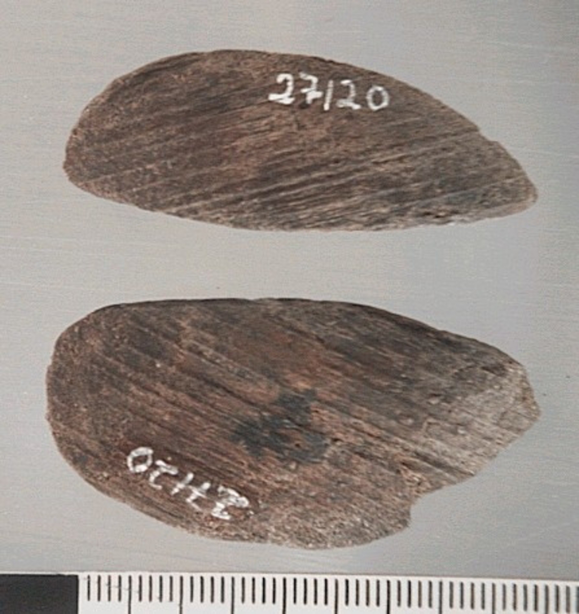 Två delar av en träsked. Delarna utgör mindre partier av skedbladet. På delarna syns en svagt rödbrun färg, vilket möjligen är spår efter bemålning.

Delarna är mycket slitna.

För mer information se Dokumentationsblankett under Referenser – Länkade filer.