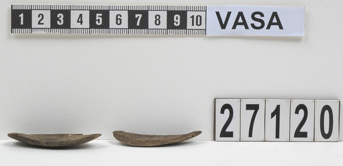 Två delar av en träsked. Delarna utgör mindre partier av skedbladet. På delarna syns en svagt rödbrun färg, vilket möjligen är spår efter bemålning.

Delarna är mycket slitna.

För mer information se Dokumentationsblankett under Referenser – Länkade filer.