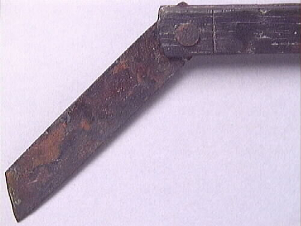 En vinkelhake, s k smygvinkel.

Skaftet är försett med sex stycken ristade skåror som markerar tum. I ena skaftänden sitter ett nytillverkat, ledat, järnblad. Bladet är fäst med en nytillverkad järnsplint. I skaftets ena ände, närmast bladet, löper en skåra eller ett spår. Spåret är mellan 68 och 80 mm djupt.

Smygvinkeln är i gott skick.

För mer information se Dokumentationsblankett under Referenser – Länkade filer.