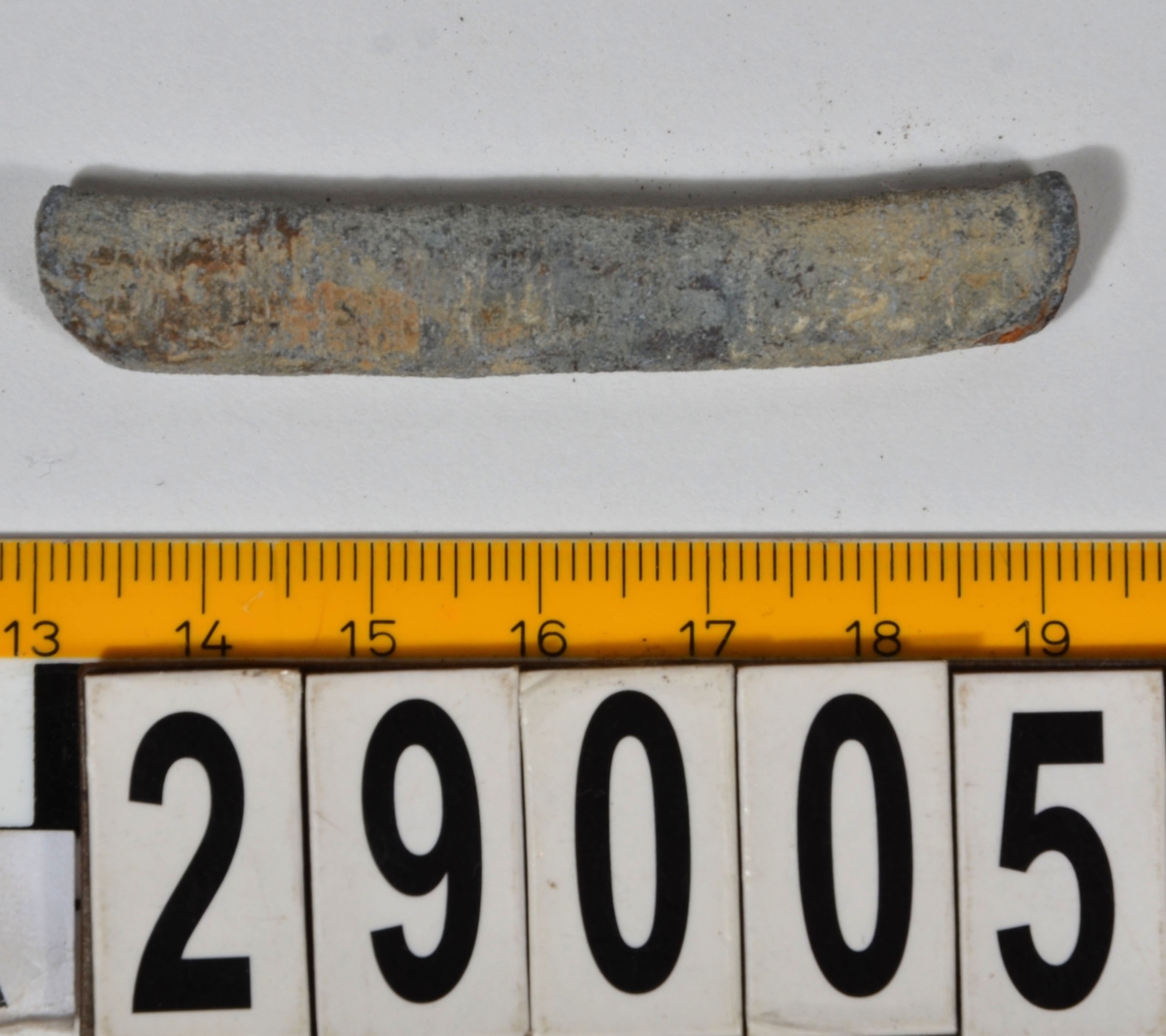 Sänket består av en vikt blybit. Sänket har tydliga märken efter det verktyg som pressat ihop sänket runt garntråden. Sänket är i gott skick.

Text in English: Lead sinker in the shape of a flat tube. The rectangular piece of lead is folded vertically in half and has visible tool marks from the folding process. The yarn is pushed through the hole. Grey mat in colour. In good condition.