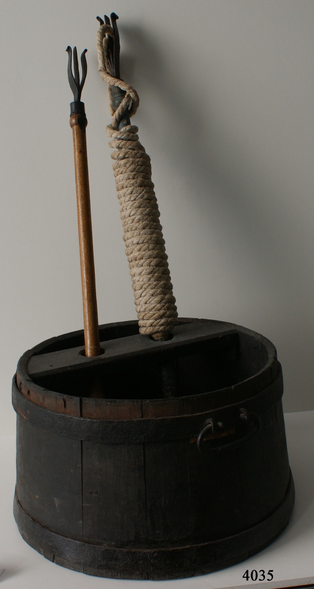 Luntbalja av trä med två järnband och två handtag av järn. Över baljan finns tvärslå med två hål för luntstakar. I botten under slån förstärkning med fördjupning för laddstakarnas ändar.