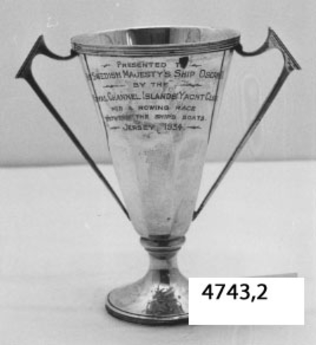 Pokal av silver. Utgör pris i rodd.
Ingravering: Presented To His Swedish Majestys Ship Oscar II By The Royal Channel Islands´ Yacht Club. For A Rowing Race Between The Ships Boats Jersey 1934 samt namnen på lagmedlemmarna.