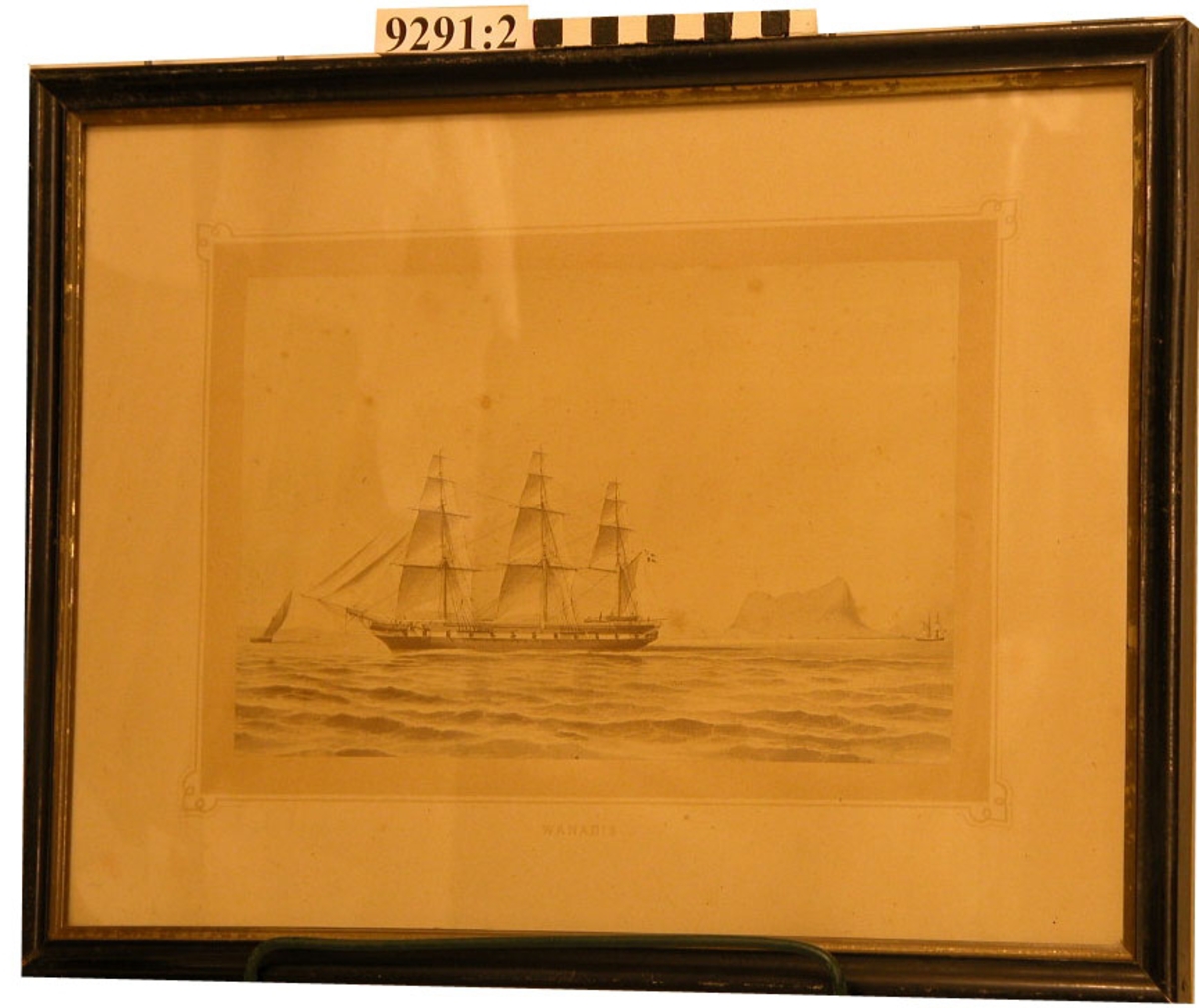 Fotografi inom glas och ram. Ramen svart med guldkanter.  Visar ångfregatten Vanadis under segel i Gibraltarsund under åren 1883-1885.