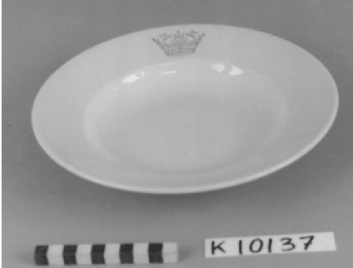 Tallrik, djup- av porslin, vitt. Dekorerad med seglarkrona i blått. Märkt i botten K  P Uppsala-Ekeby Karlskrona III.