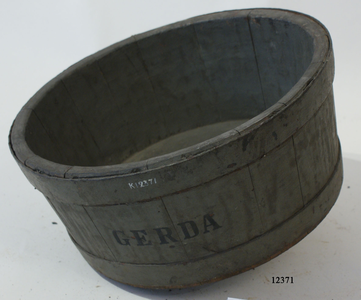 Tratt av ekträ. Cylindrisk, svagt konad innåt. Botten plan med hål i centrum med rör av koppar, vartill är fäst en fläns, fastnitad till botten. Runtom två järnband. Tratten gråmålad. Märkning: GERDA.