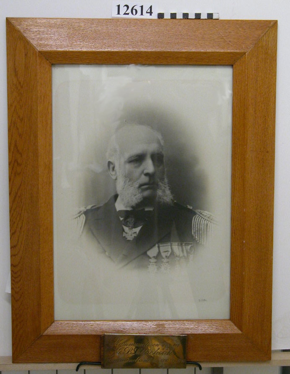 Personfotografi inom glas och ram av ek. Text på namnplåt av försilvrad mässing: Kommendören  m.m. G. B. Lilliehök Kommendant 1/10 1890-30/9 1893.
Neg.nr 4936-4947