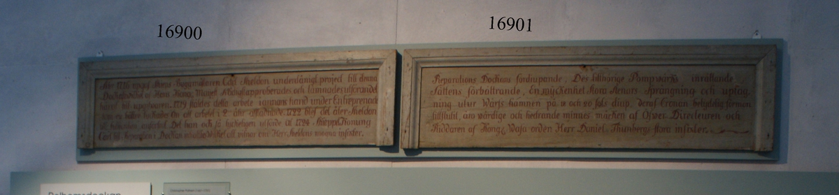 Minnestavla av trä, gråmelerad på framsidan, med rödmålad text rörande tillkomsten av Gamla Dockan på Lindholmen, Karlskrona örlogsvarv, till åminnelse av Charles Sheldon.
 Inom profilerad ram (saknas på nedre delen) 60 mm bred. Baksidan är gråmålad.