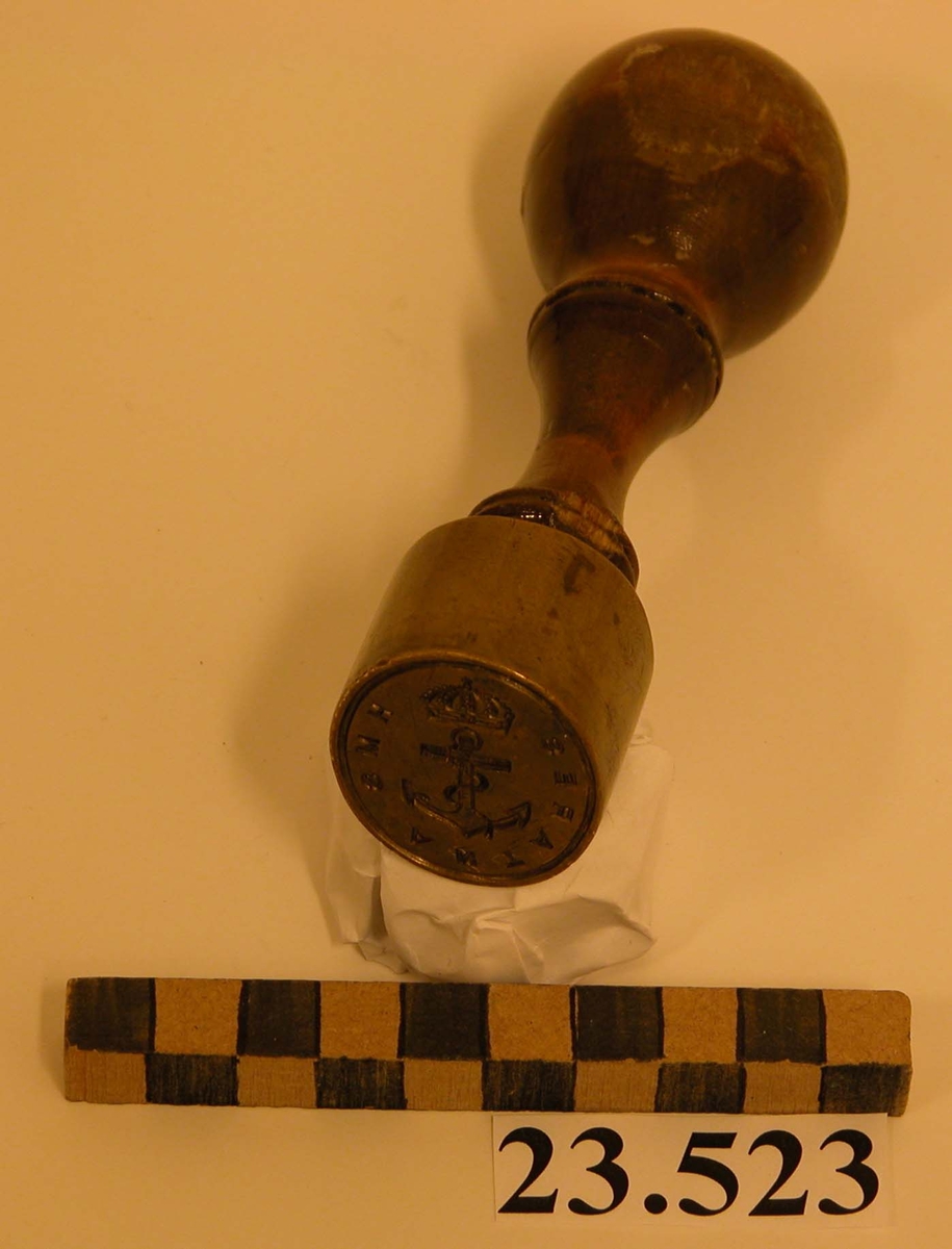 Lacksigill med stans av mässing, oval form. Svarvat och lackat ljust träskaft, löstagbart. Text: (negativt i sigillet). I mitten krönt stockankare, längs kanten: HMS ANTARES. Det hela inom en ring.