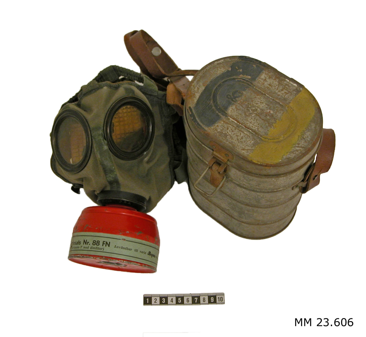 Gasmask 2 st. Gasmasken består av: Ansiktsskydd med ventilhus och behållare. Ansiktsskyddet är av gastätt grönt gummerat tyg. Det är försett med infalsade ögonglas. Tätningsram av skinn för tätning mot ansiktet, bandställ med elastiska band för gasmaskens kvarhållande på huvudet samt gängad rund ventil av metall för anslutning av behållare. På den gängade ventilen text: Degea D.R.P. 2. Masken är stämplad på insidan: 23 Juli 1929,  2, 747. Masken förvaras i behållare av metall, oval form (slitet). Lock på gångjärn samt knäpplås. På locket text: Degea samt två målad linjer, en gul och en svart. Reglerbart bärband av läder. I behållaren finns även ett gasfilter, rött med guldfärgat påskruvat lock. Grön pappersremsa längs behållaren med text: Degea filterinsats Nr.88 FN (Brandkårsinsats F med dimfilter) Användbar till varje Degea-mask, Provad: 26.3.36. Se SSS och X pärm.
