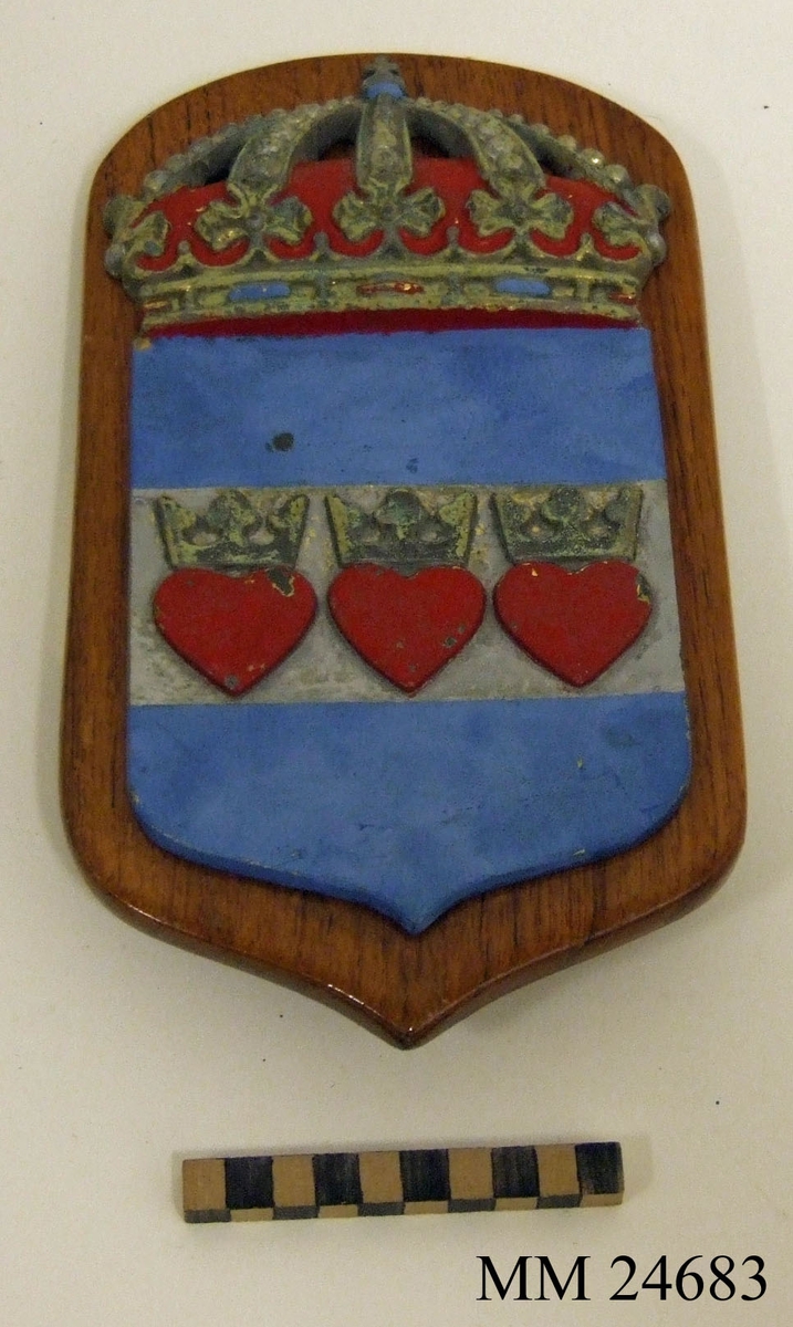 Vapenskölden består av Halmstads stadsvapen i metall fäst på en träplatta. Stadsvapnet  är ljusblått. Ungefär mitt på går en grå rand och i den sitter tre hjärtan med kronor på. Skölden kröns av en kungakrona. På baksidan finns fästanordningar i metall.