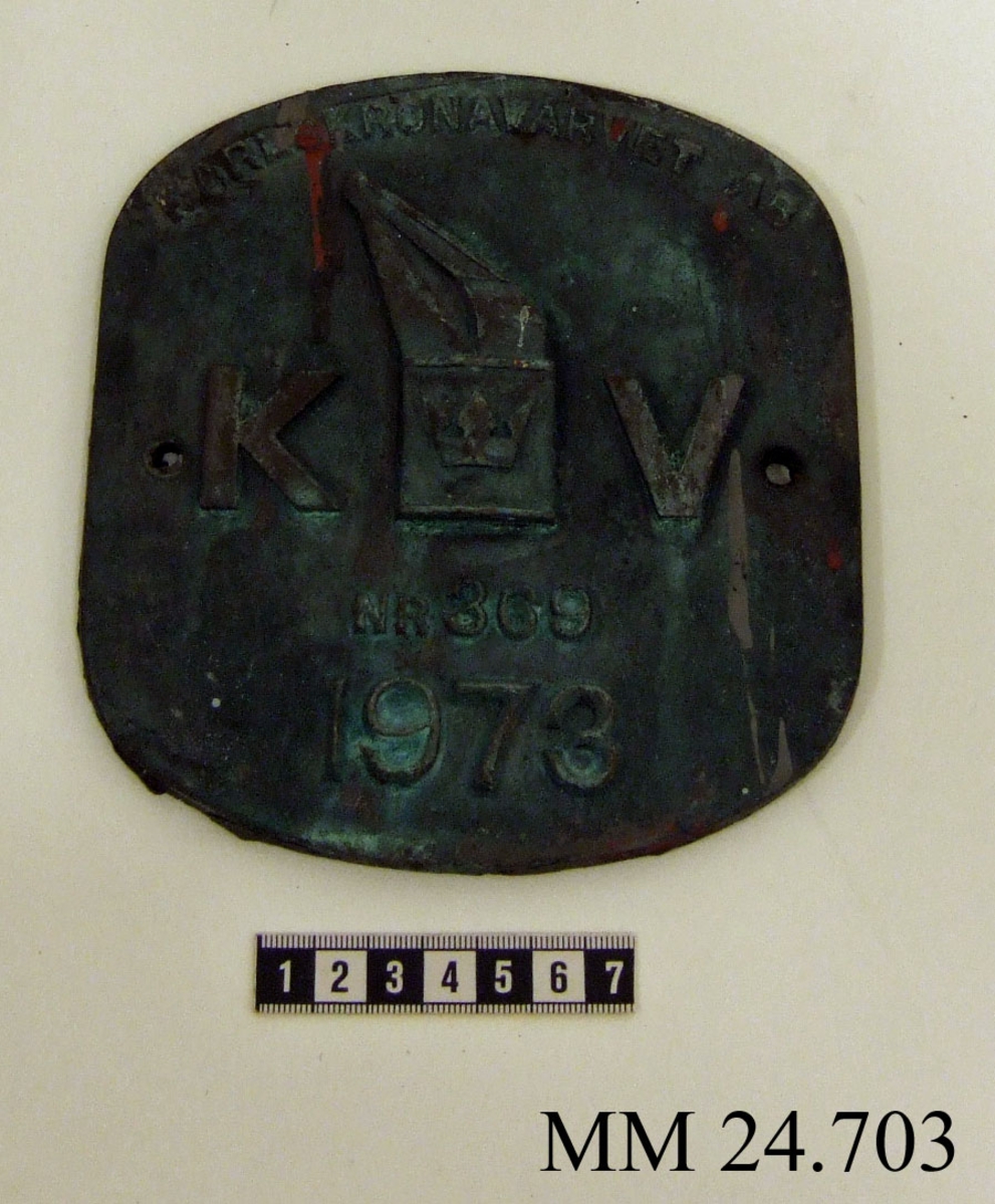 Metallskylt med inskription i relief. Texten på skylten lyder: Karlskronavarvet AB KV NR 369 1973. I mitten, dvs. texten KV, utformad som Karlskronavarvets logotype. Hål borrat i varje långsida.
