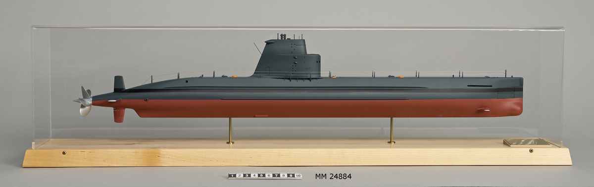 Ubåtsmodell Draken II i monter. Modell av alträ med detaljer av mässing, målad med cellulosafärg. Rött och svart skrov. Monter av plexiglas på träplatta. Mässingsbricka i montern med uppgifter om modellen.