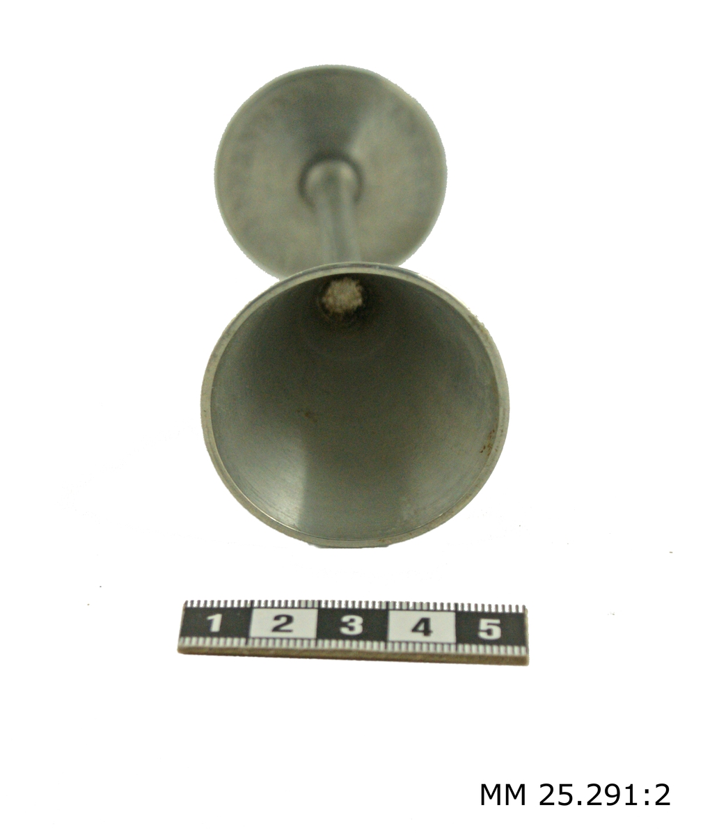 Snapsglas i tenn på fot. Övre delen konformad, övergår genom en skarv till en rak pinne som genom ytterligare en skarv övergår till en svagt konformad cirkelrund fot.
Stämplat på fotens undersidan: "GJUTEN I KALMAR AV  RUNE TENNESMED O10".