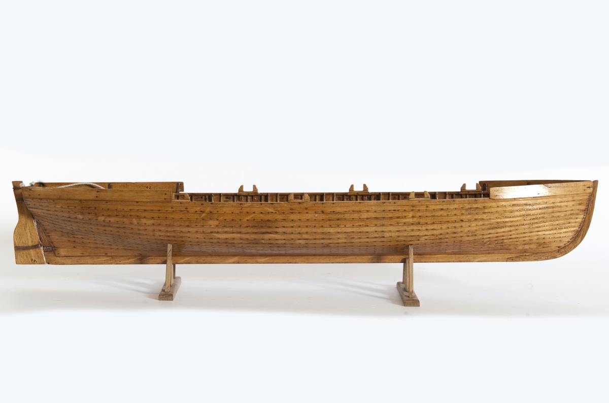 Gigg, bordlagd på spant, klink med fullständig inredning. 6 årtullar, 6 åror. Roder med skädda. Fernissad, Stativ fernissat. Masten saknas.