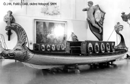 In 1783 King Gustaf III travelled to Italy. In Venice he was taken on a tour in a gold-ornamented gallery. The king also watched a splendid spectacle in the form of a regatta on the Canal Grande. A great number of decorated boats and gondolas assembled well before noon. At two o'clock in the afternoon boats with Venetian nobelmen came to pick up the king and his entourage to see the regatta. The boats were decorated with silk, canopies, parasols and flowers. The rowers were dressed in silk and adorned with silver. "The spectacel was vivid, full of splendor and distinctive character and quite dazzling", as Gundmund Jöran Adlerbeth writes in his diary from the journet. King Gustav III was very much impressed.

I order to supreise the king, master ship builder Fredrik Henrik af Chapman had "two pleasure vessels for Haga" built. Haga was a rural ground, north of Stockholm, where Gustav III at the time was creating a royal rank park. The "gondolas" were probably built in 1785 or 1786, and the heads of the boats were in all certainty made by the sculptor Hohan Törnström.

The king was "infinitley pleased", and the sloops came to be used frequently on the Brunnsviken and off Drottningholm. For rowing, boatsmen commandeered from the navy were used. The boar have been called sloops, pleasure vessels or gondolas depending on where they mentioned. The shields were originally 24 in number, with motifs from antiquity and from the twelve labors of Heracles.

After the assassination of Gustav III the sloops were forgotten and rarley used until they were pun into service again for a while during the reign of Karl XV (1859-1872). Since then, they have been stored at various places, e g near the copper tents at Haga, on Skeppsholmen and, since 1966, in the collections of the National Maritime Museum.    