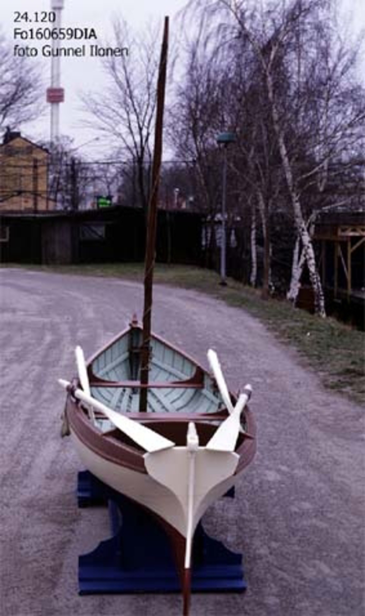 Roddgigg, kravellbyggd roddbåt i furu.
Längd 4,5 meter.
Bredd 1,05 meter.
Denna lilla och långsmala roddbåt, är som skylten i aktern anger, byggd vid Långholmswarfvets Båtvarf i Stockholm.
Den inköptes den 8 juni 1891 av mekanikern KA Karlsson på Stockholms Stads Auktionsverk för 56 kronor och 25 öre.
Att båttypen kallas för gigg beror på att den är försedd med ett roder som styrdes av en person på aktertoften.
Giggar fanns ombord på större fartyg och användes ofta i Flottan för att transportera iland befäl.
Denna gigg har dock använts uteslutande som fritidsbåt.

Tillbehör: 3 tofter. 2 par åror och årklykor. 6 durklappar. Roder med rorkult.
2 skäddor för giggstyrning. 4 hjärtformade fendrar.