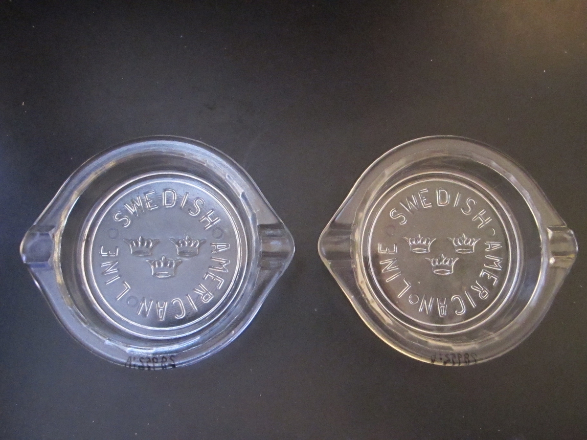 Askkoppar i pressglas. Runda med fasettmönstrade sidor, tunn kant upptill med två "cigaretthållare". Gjutet mönster på undersidan av den genomskinliga botten: "SWEDISH AMERICAN LINE" i cirkel kring SAL:s emblem med tre kronor.